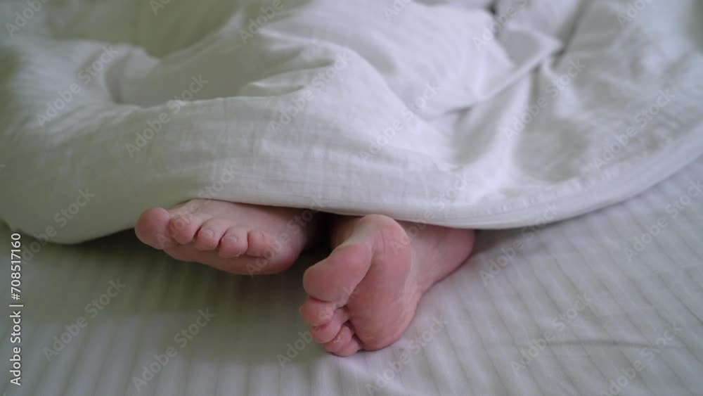 legs of an unknown person under a blanket in bed, Bare feet middle-aged woman peeking out from under blanket legs of an unknown person under a blanket in bed, Bare feet middle-aged woman peeking out from under blanket