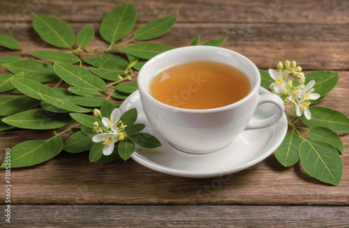 Healthy Lifestyle Concept with Moringa Tea in white ceramic cup. Fresh green leaf and Flower on Wooden Background