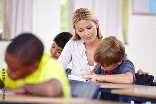 Teacher, kid or writing in classroom for learning, education and helping for language development or support. Woman teaching, assessment or child student with knowledge or notebook at middle school