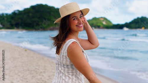 Young attractive woman smiling and walking on the beach at sunrise on her tropical vacation, happy white woman enjoying the beach
