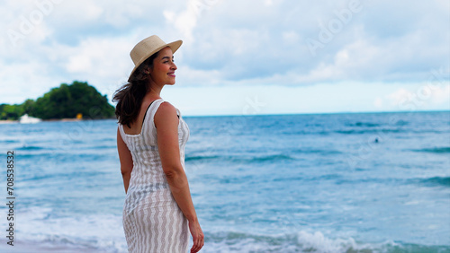 Happy young white woman wearing hat feeling the sea breeze. Beautiful smiling girl relaxing and enjoy the sun at seaside. 