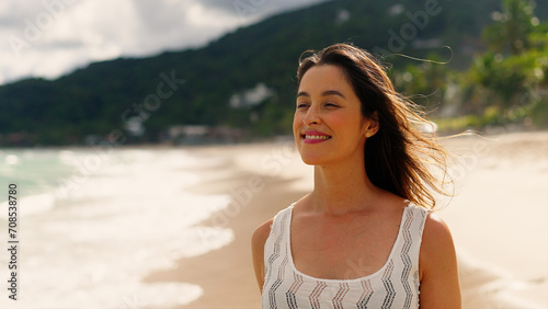 Happy Woman walks along sandy beach with ocean behind. 