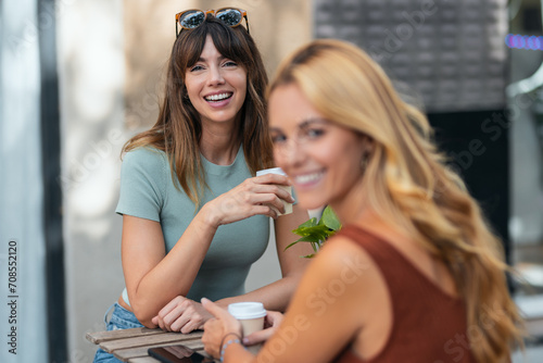 Two attractive friends enjoying coffee together while talking and laughing sitting on the terrace of a bar.
