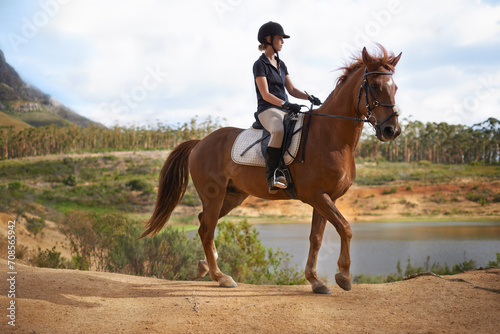 Equestrian, woman and riding a horse in nature on adventure and journey in countryside. Ranch, animal and rider outdoor with hobby, sport or walking a pet on farm with girl in summer at river © Tasneem H/peopleimages.com