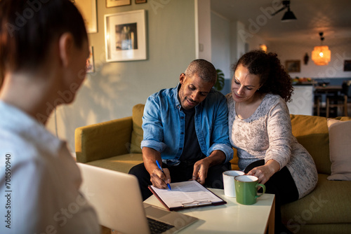 Couple signing documents at home with consultant photo