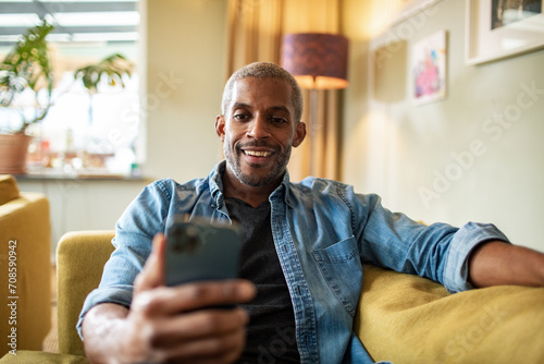 Smiling man using smartphone on couch at home photo