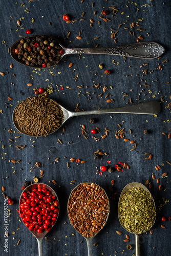 Old metal spoons with different kind of spices on black background