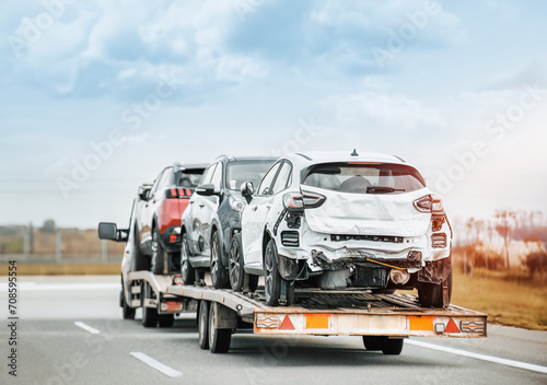 Rear view of tow truck transporting 3 totaled damaged cars. Car insurance paid off the actual cash value ACV. Car restoration after being totaled. Car auctions. © AlexGo