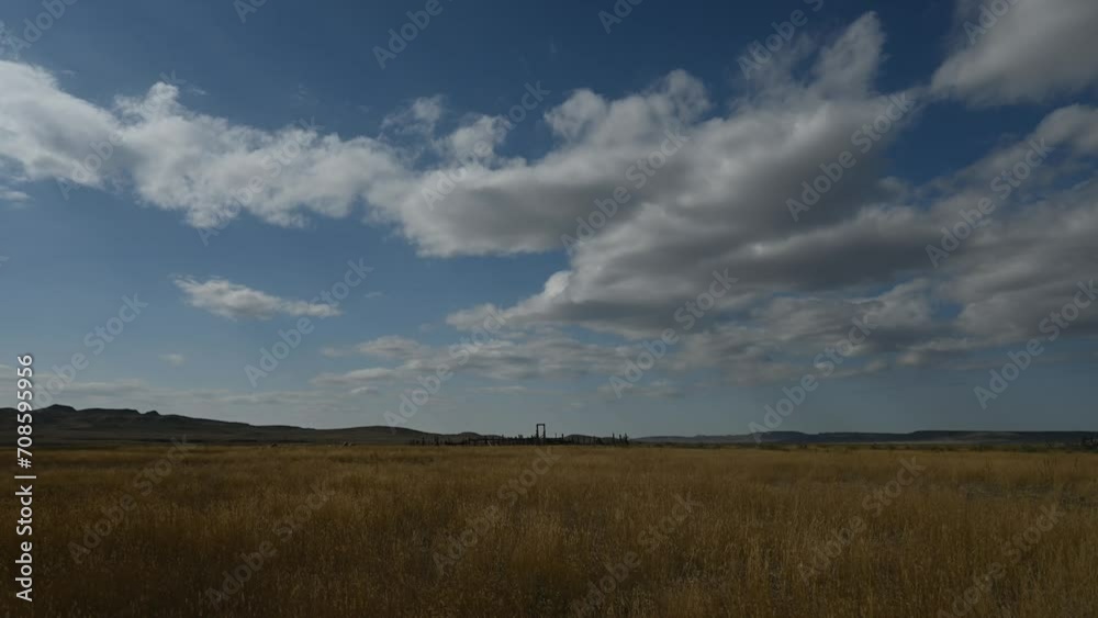 Time lapse of white clouds moving through a blue sky above a prairie landscape with rolling hills in the background. The fall colored grass moves in a light wind.
Time lapse of white clouds moving through a blue sky above a prairie landscape with rolling hills in the background. The fall colored grass moves in a light wind.