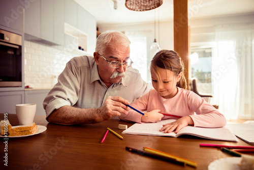 Grandfather helping granddaughter with drawing at home © Vorda Berge