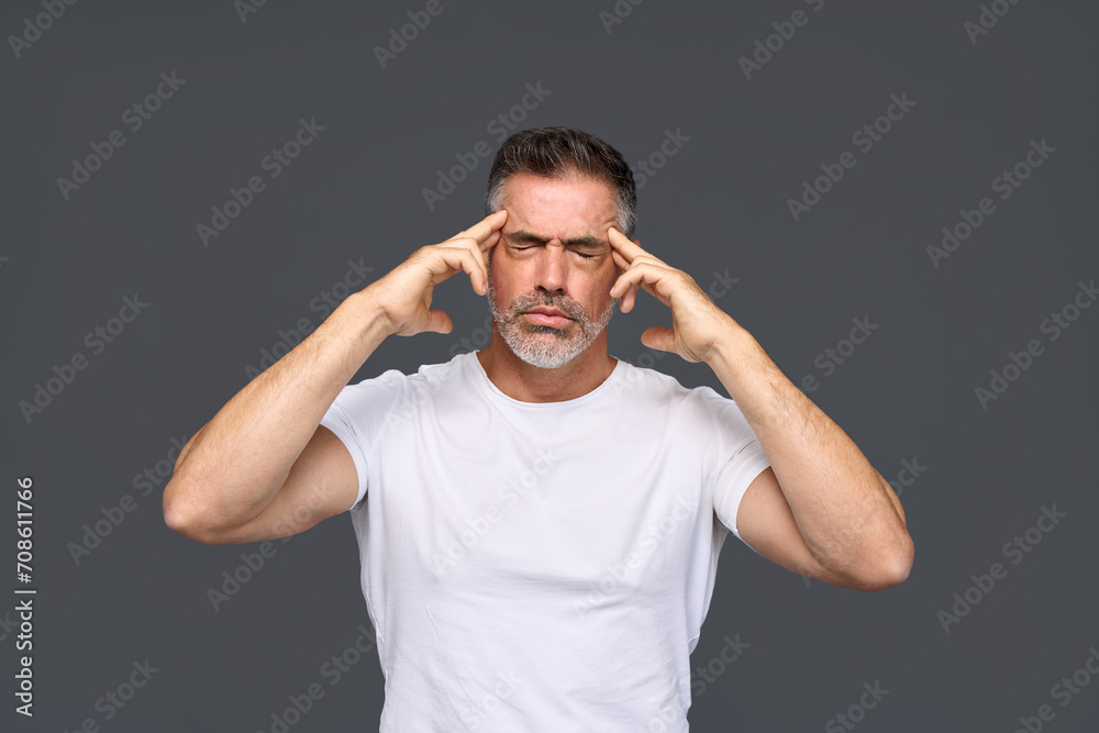 Unhappy stressed older man, annoyed sad middle aged male model wearing white t-shirt feeling pain having severe headache or migraine touching head standing isolated on gray background.