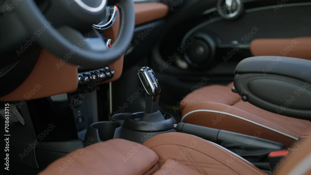 Interior of city sports car Mini Cooper S Convertible with front seats in brown leather and dashboard details. Steering wheel and speed shifter of classic vehicle
