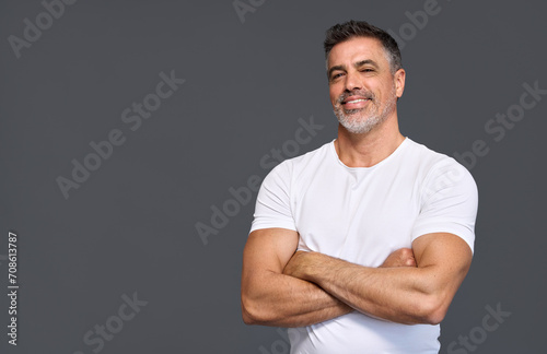 Happy fit sporty older man coach, middle aged sportsman athlete or personal trainer wearing white t-shirt showing muscles standing isolated on gray background advertising gym membership. Portrait. photo