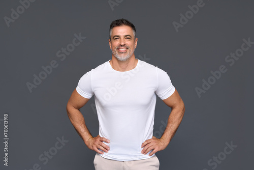 Happy confident handsome fit sporty healthy mature older man, middle aged sportsman athlete or personal trainer wearing white t-shirt standing isolated on gray background advertising gym. Portrait