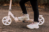 A girl, a child in sneakers rides on a pink scooter on the asphalt in the fall. Photography, sports, legs close-up.