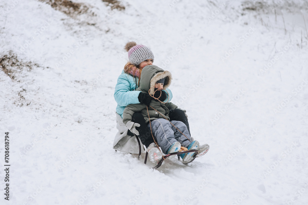 A little boy with his sister's girl, happy children, a family, sitting together on a sled, going down a hill in the snow in winter. Photography, portrait, childhood concept, lifestyle. A little boy with his sister's girl, happy children, a family, sitting together on a sled, going down a hill in the snow in winter. Photography, portrait, childhood concept, lifestyle.
