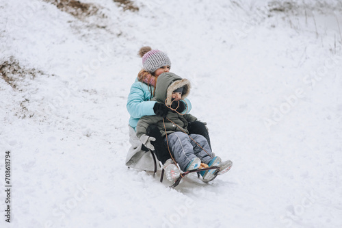 A little boy with his sister's girl, happy children, a family, sitting together on a sled, going down a hill in the snow in winter. Photography, portrait, childhood concept, lifestyle.