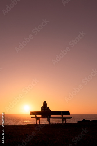 Woman sitting on a bench enjoying the sunset on the beach - Adventure travel concept