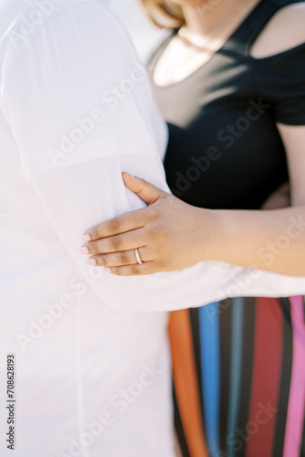 Woman put her palm on the arm of man hugging her waist. Cropped. Faceless