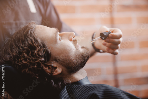 Barber applies oil with dropper for beard man in barbarshop. photo