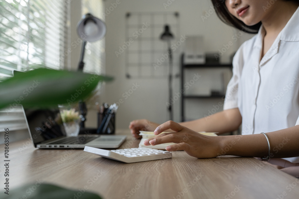 woman working at home in the living room with note, counting on a calculator, paying bills, planning a budget to save some money