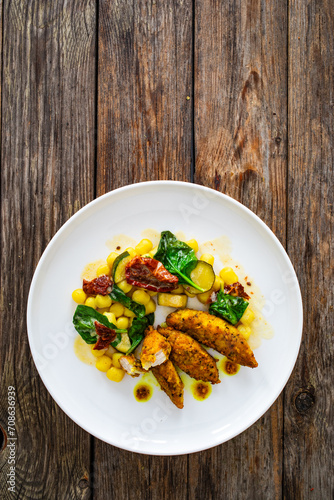 Fried chicken breast fillet with gnocchi and sun dried tomatoes on wooden table
