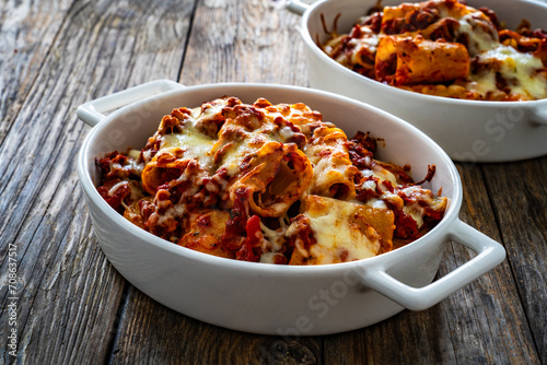 Paccheri con ragù alla bolognese casserole - roasted noodles with bolognese sauce and mozzarella cheese on wooden table
