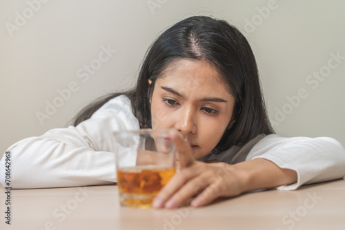 Alcoholism drunk asian young woman hand holding glass of alcohol or whiskey, female sitting alone, drinking on table at home, at night. Treatment of alcohol addiction, suffer abuse problem alcoholism