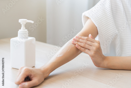 Health care, beauty smile pretty asian young woman in bathrobe, towel after shower bath at home, hand applying, putting moisturizer on her arm. Skin body cream moisturizing lotion, routine in morning.