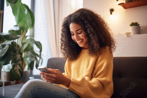 Happy young latin woman sitting on sofa holding mobile phone using cellphone technology doing ecommerce shopping, buying online, texting messages relaxing on couch in cozy living room, Generative AI photo