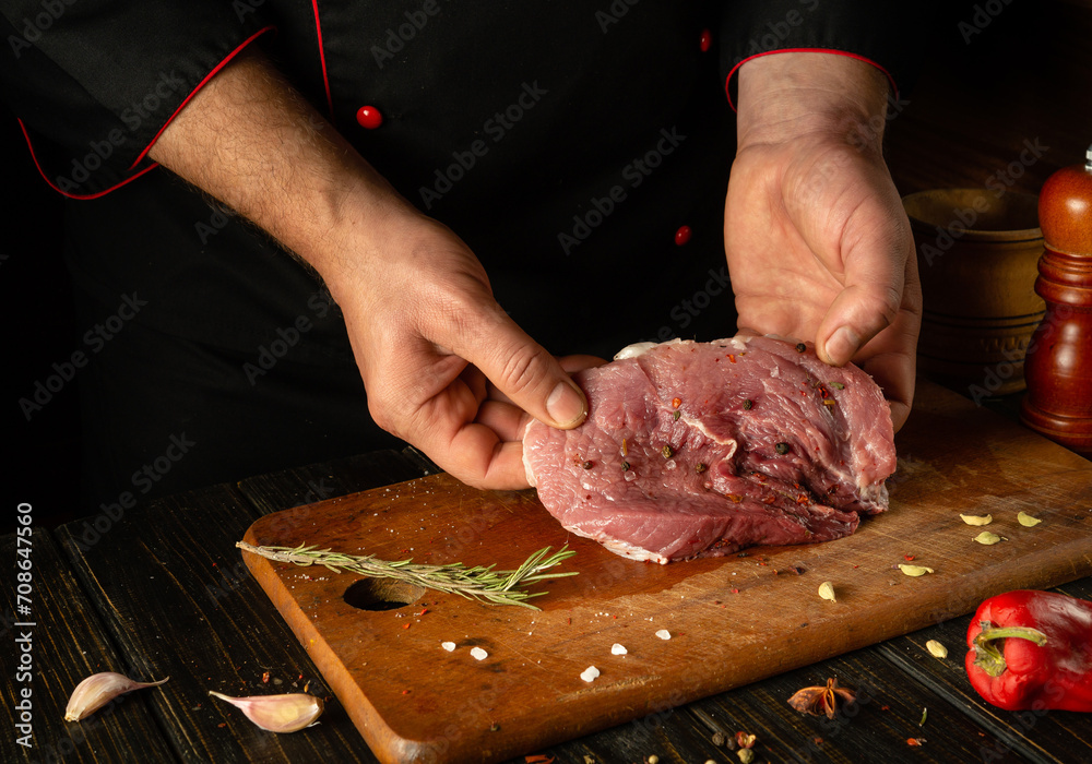 The cook is preparing a barbecue of veal steak on the kitchen table. Chef's hands with a cut piece of meat