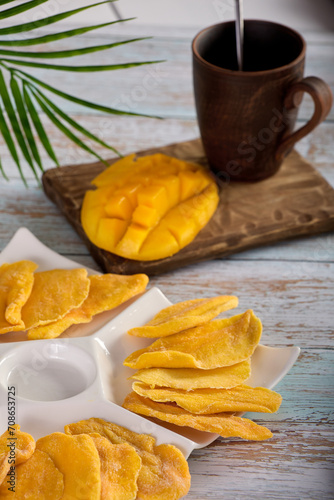 Fototapeta Naklejka Na Ścianę i Meble -  Bright delicious yellow mango beautifully served on white porcelain dishes. Close up of delicious mango fruit is laid out on beautiful white plate, dried and juicy, fresh with tropical green leaf. 