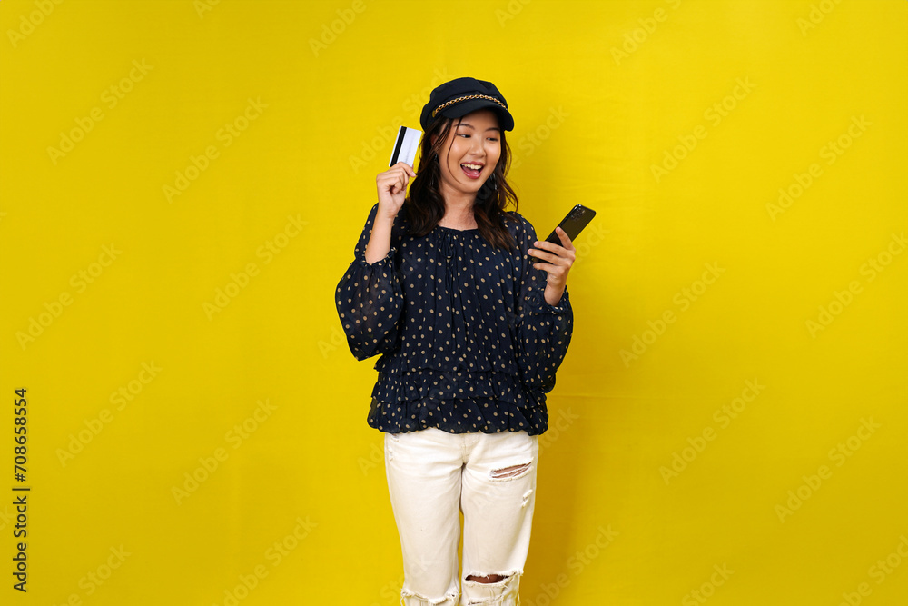 Online shopping concept. Woman holding credit card and looking at smartphone app, buying, order delivery in mobile phone application, standing over yellow background Online shopping concept. Woman holding credit card and looking at smartphone app, buying, order delivery in mobile phone application, standing over yellow background