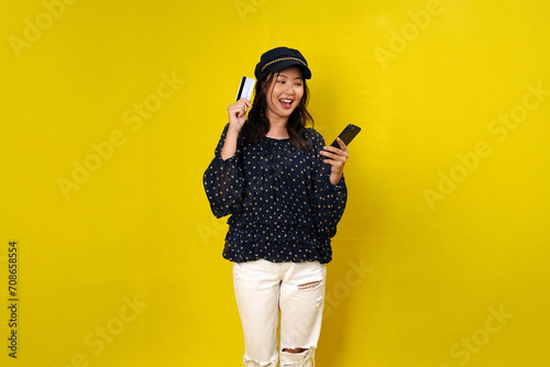Online shopping concept. Woman holding credit card and looking at smartphone app, buying, order delivery in mobile phone application, standing over yellow background © Daniel Pawer