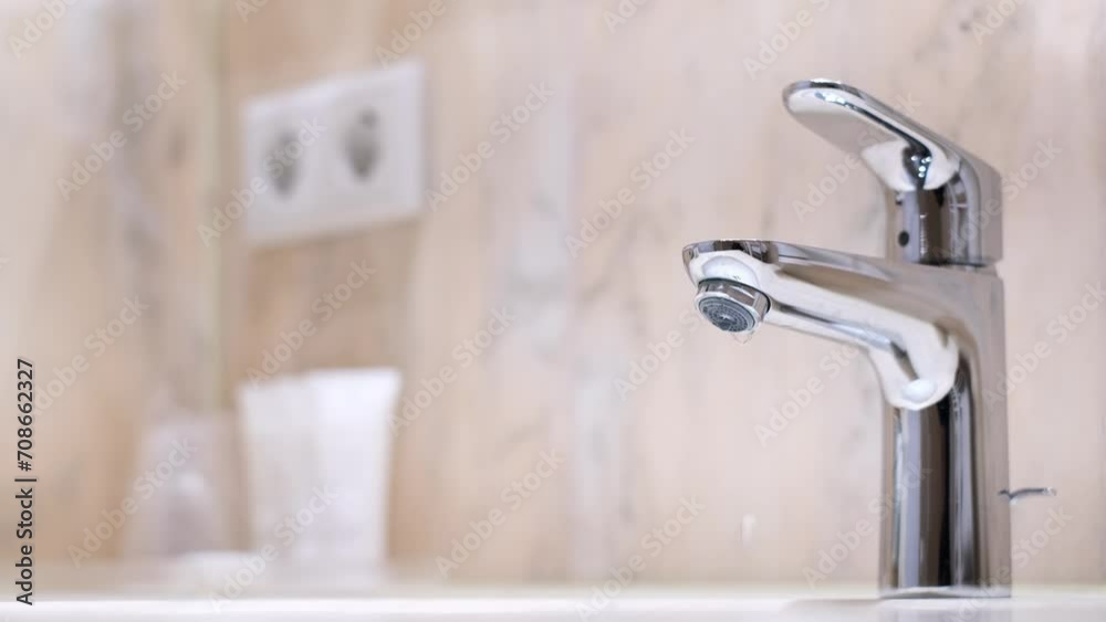 Drop of water drips from the tap. Beautiful fresh and clean water flowing from a tap. Close-up slow motion broken chrome faucet in the bathroom. Everyday problems, wasting water and energy. Drop of water drips from the tap. Beautiful fresh and clean water flowing from a tap. Close-up slow motion broken chrome faucet in the bathroom. Everyday problems, wasting water and energy.