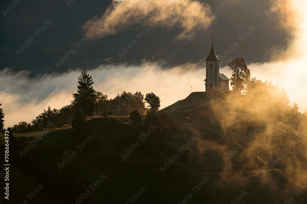 Jamnik, Slovenia - Magical foggy golden summer sunrise at Jamnik St.Primoz church. Jamnik, Slovenia - Magical foggy golden summer sunrise at Jamnik St.Primoz church.