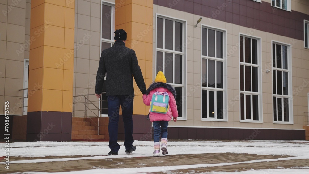 caring parent takes little girl school, little child goes school, child holds his father hand, view from back, school snowy road, child jacket boots walks cold snow school, daughter dad happy family,
