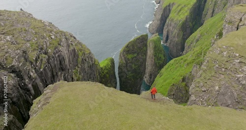 Aerial Shot Of Male Tourist Walking On Top Of Green Mountain, Drone Flying Forward Towards Birds Flying Over Sea - Faroe Islands, Denmark