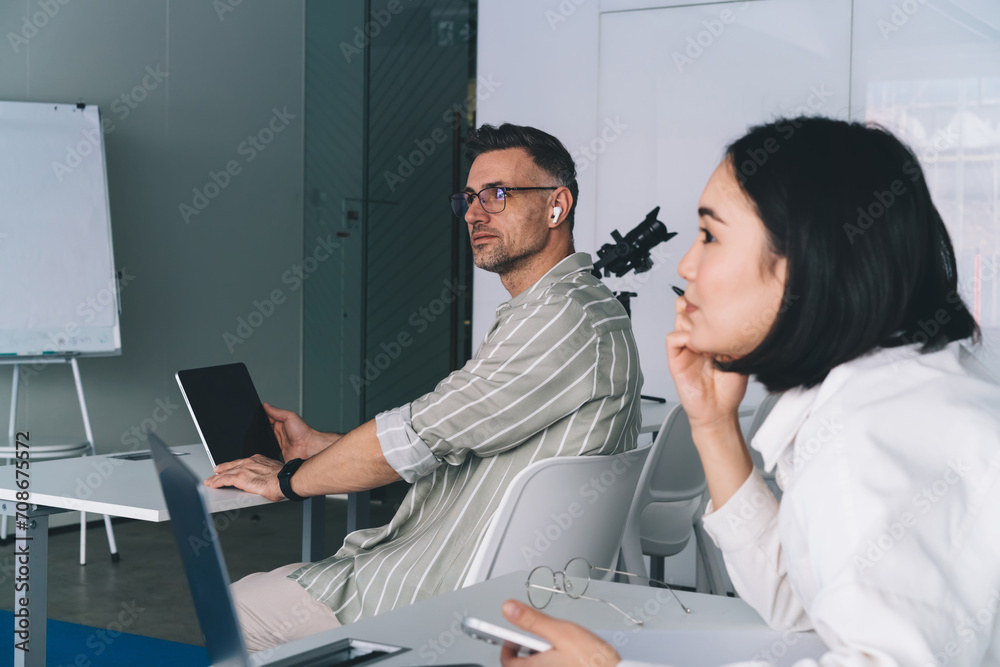 Obraz premium Side view of male and female colleagues with modern technologies thinking about marketing business during collaboration meeting in office interior, professional executive managers in workspace