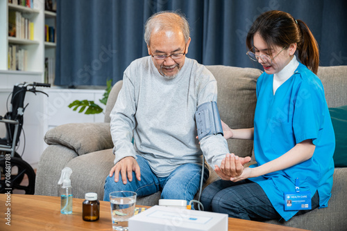 Asian doctor woman examine do checking old man client heart rate with pulsimeter monitor, nurse visit patient senior man at home she measuring arterial blood pressure on arm in living room, Healthcare photo