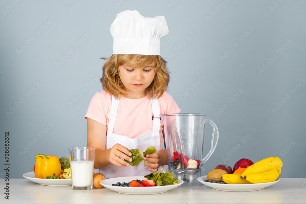 Child chef cook prepares food on isolated grey studio background. Kids cooking. Teen boy with apron and chef hat preparing a healthy vegetables meal in the kitchen. Child chef cook prepares food on isolated grey studio background. Kids cooking. Teen boy with apron and chef hat preparing a healthy vegetables meal in the kitchen.