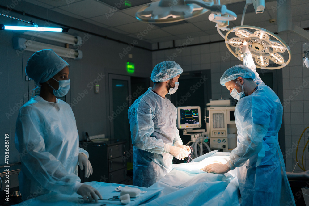 Male doctor in surgical uniforms and masks adjusting light before operation in dark operating theatre. Surgery, hospital, medical and healthcare services. Concept of surgery and emergency. Male doctor in surgical uniforms and masks adjusting light before operation in dark operating theatre. Surgery, hospital, medical and healthcare services. Concept of surgery and emergency.