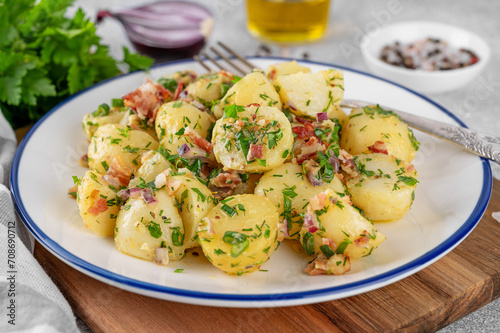 Warm potato salad with bacon, onion, fresh herbs and vinegar dressing in a bowl on a gray concrete background. German Kartoffelsalat.