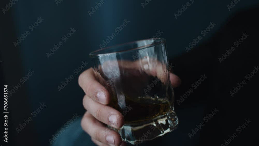 A man in a suit holding a glass of whiskey, with a focus on the hand and the watch, against a dark, blurred background, suggesting sophistication. A man in a suit holding a glass of whiskey, with a focus on the hand and the watch, against a dark, blurred background, suggesting sophistication.