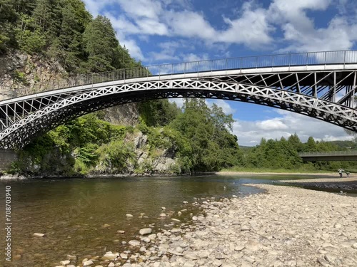 A beautiful steel bridge crosses over the river Spey in Scotland as seen from the pebbled shores below where rock throwing awaits.