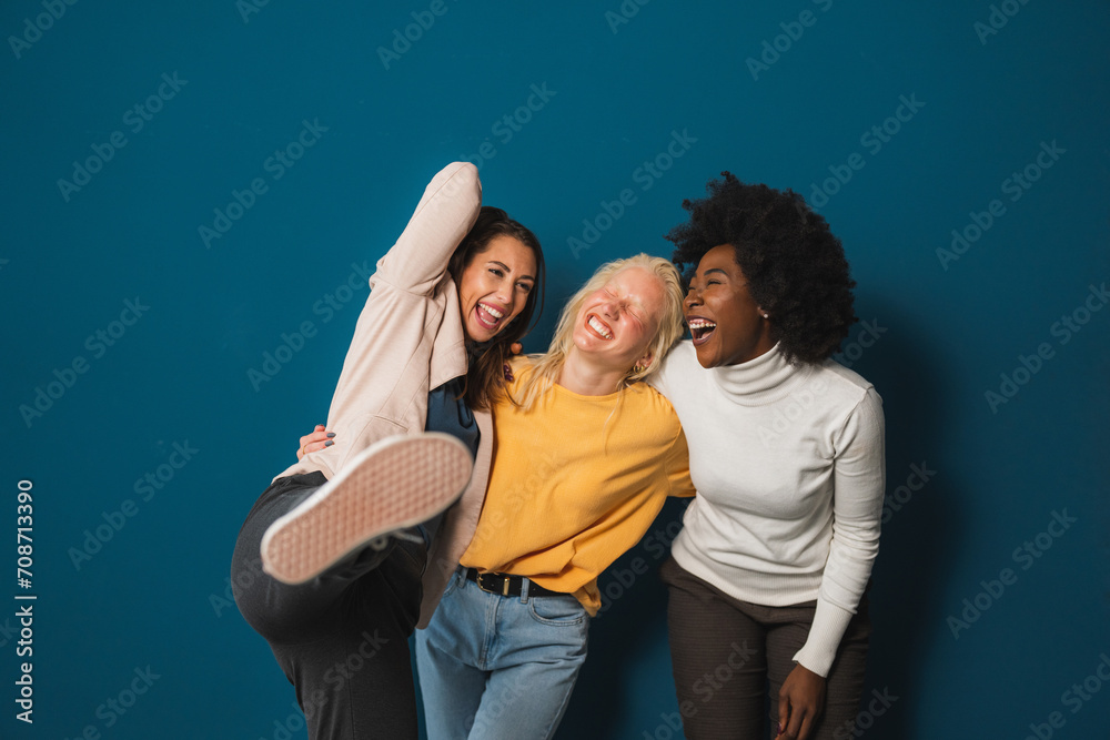 Group of cheerful female friends having fun while embracing each other. Three happy young women laughing and having a good time while standing against a studio background. Group of cheerful female friends having fun while embracing each other. Three happy young women laughing and having a good time while standing against a studio background.