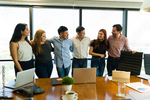 Group of businesspeople in casual clothes embracing each other and looking happy