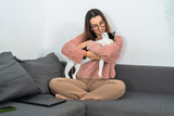 A loving woman in a cozy sweater cuddles her black and white cat on a sofa, sharing a moment of affection.