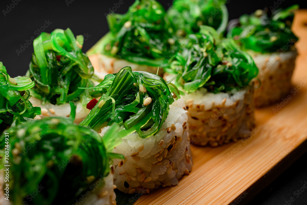 Portion of sushi rolls with a pile of green algae, close up