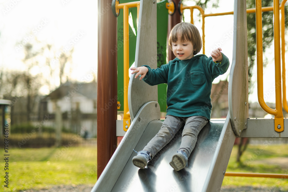 Fototapeta premium Cute toddler boy having fun on a playground outdoors on warm summer day. Active leisure for kids.